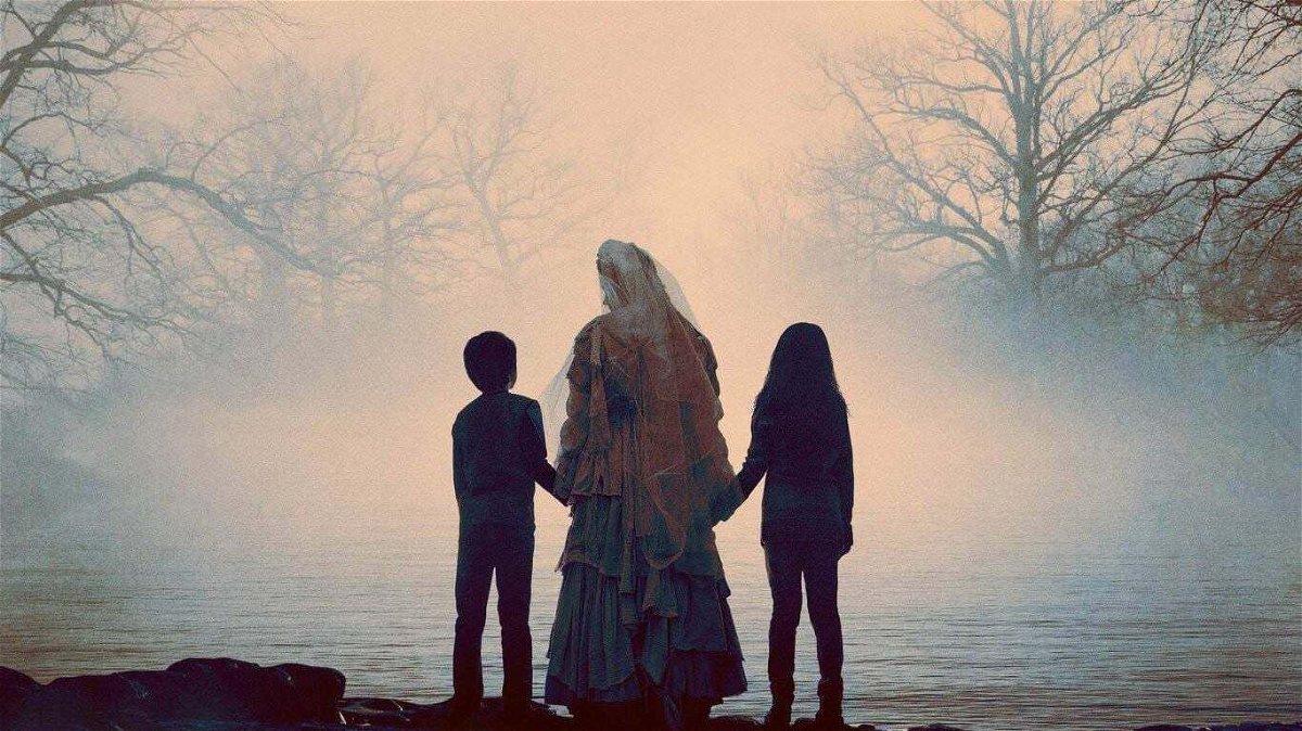 La Llorona, di spalle, conduce un bambino e una bambina verso un lago immerso nella nebbia