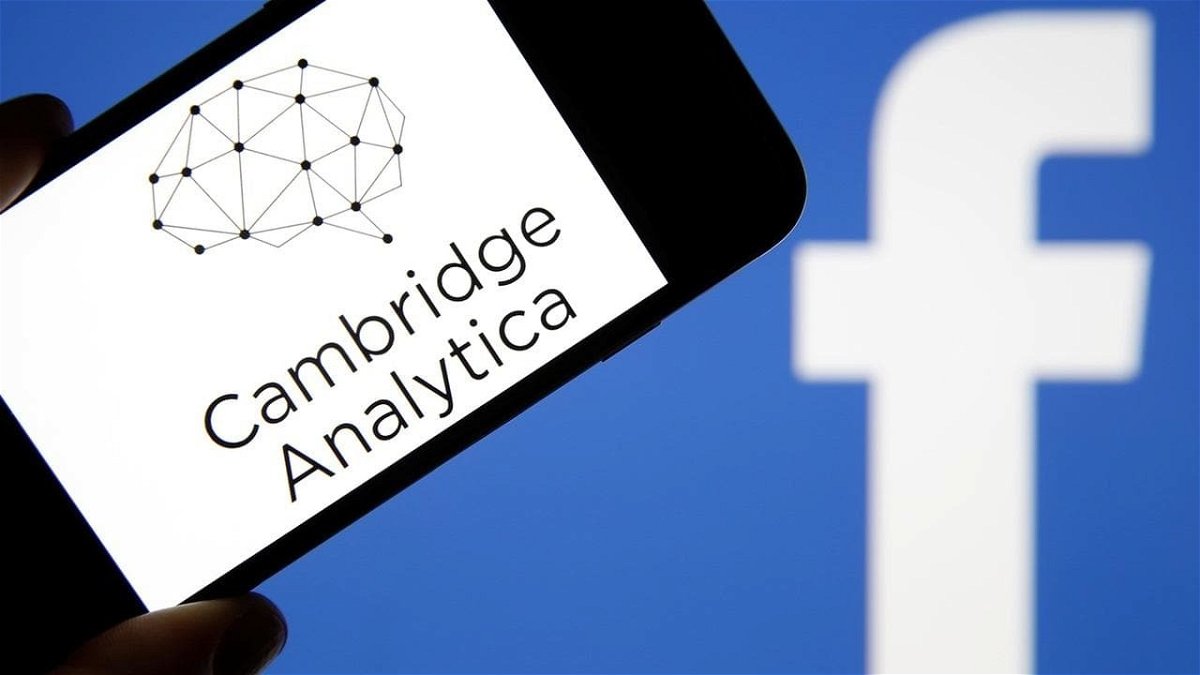 Primo piano del logo di Cambrige Analytica e sullo sfondo quello di Facebook