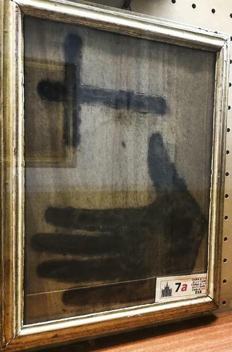 Una tavola di legno dove sono presenti le impronte di una mano e il disegno di una croce 