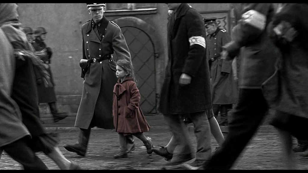 Su uno sfondo completamente in bianco e nero spicca una bambina in cappotto rosso portata via dai tedeschi