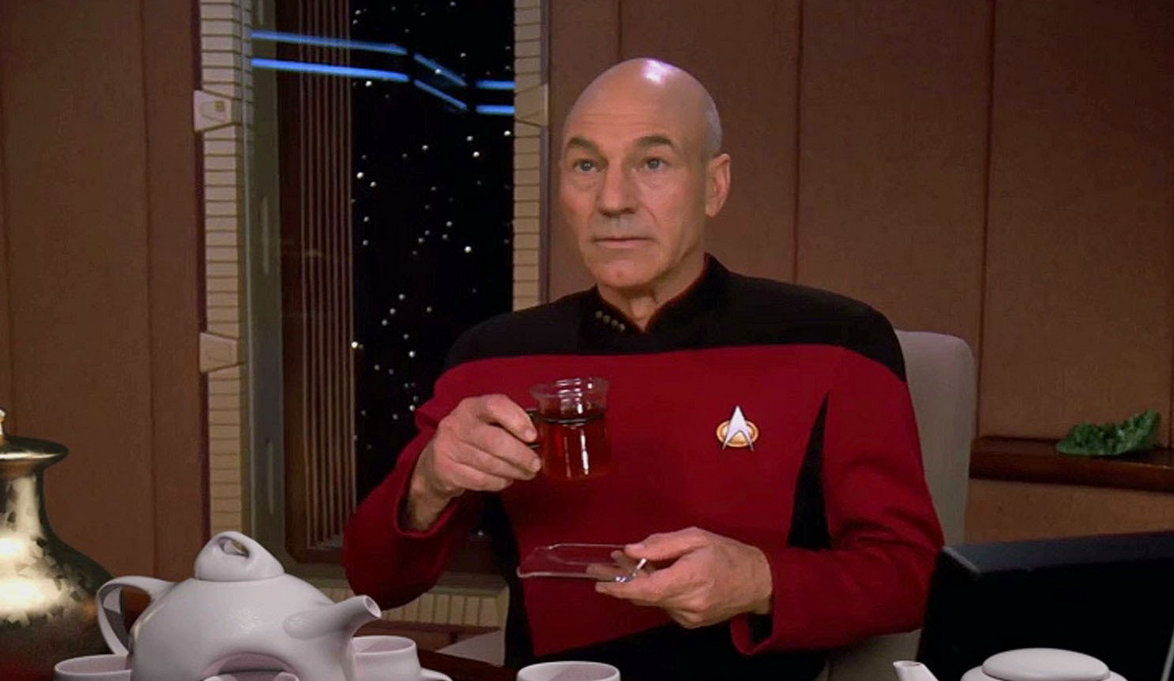 Mezzobusto di Patrick Stewart con l'uniforme di Picard, seduto alla scrivania del suo ufficio sull'Enterprise