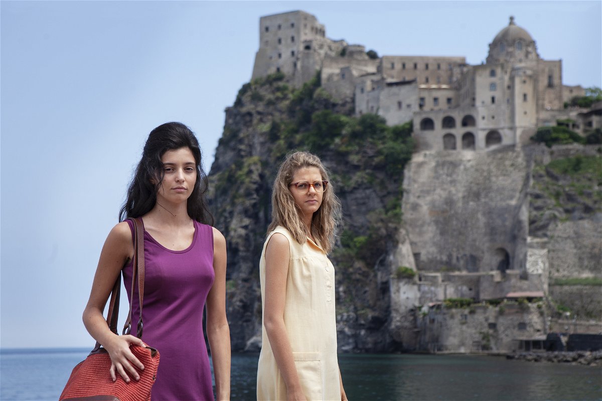 Lila ed Elena guardano la telecamera, sullo sfondo il Castello Aragonese di Ischia