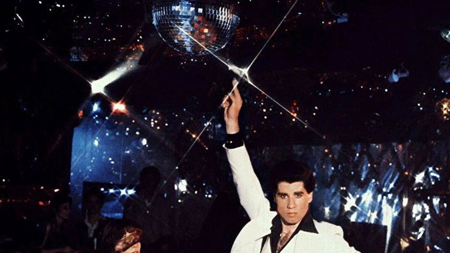 John Travolta in completo bianco alza il braccio sulla pista da ballo