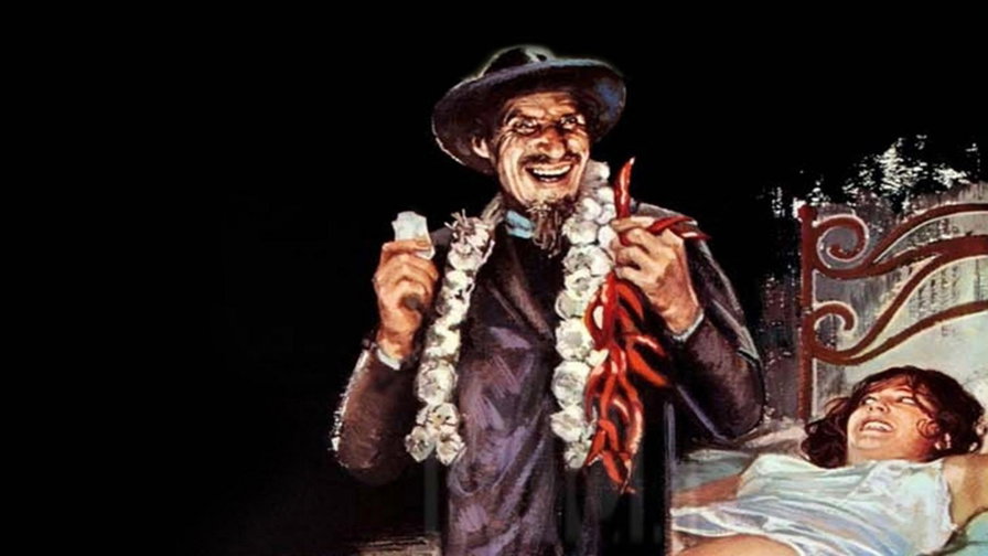Ciccio Ingrassia con un cappello e una collana di fiori accanto a una donna distesa